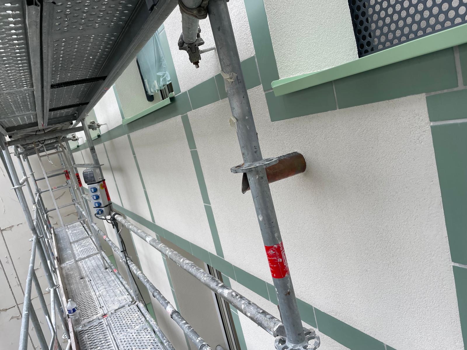 Travaux sur la façade blanche et verte depuis l'échafaudage