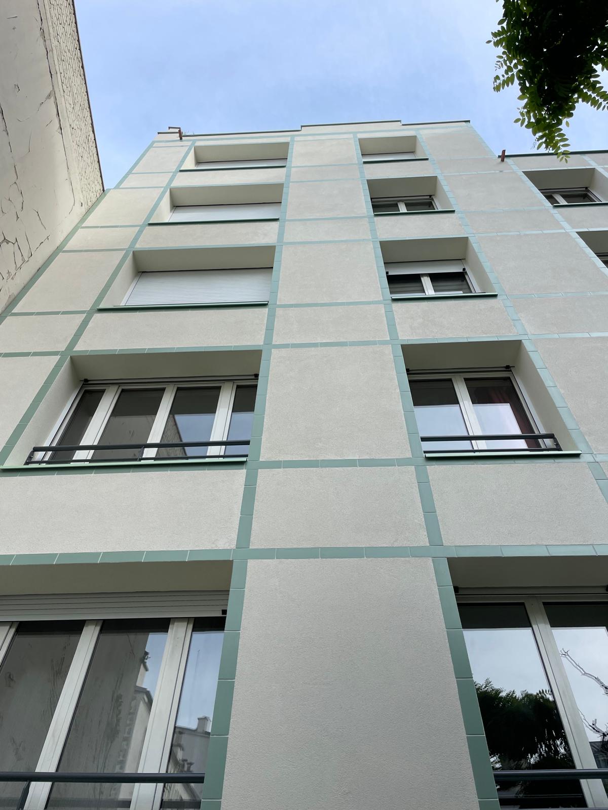 Façade rénovée d'un immeuble, enduit blanc et encadrements verts